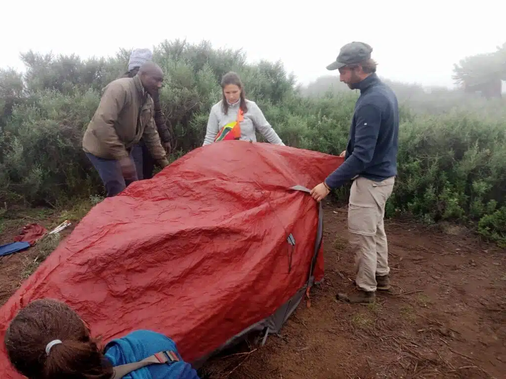 Gemfinders Safaris guests setting up a red tent during a guided hike on Mount Kenya, promoting low-impact, sustainable travel