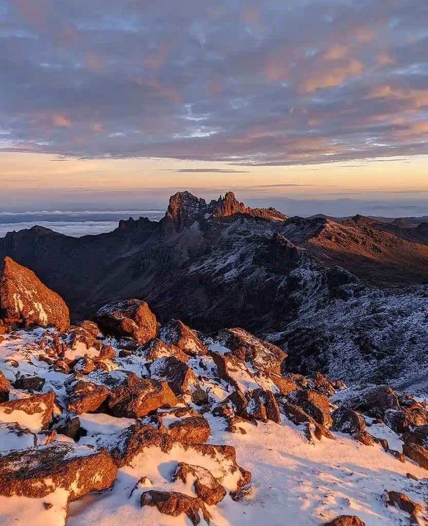 A panoramic view of Mount Kenya’s rugged peaks, bathed in early morning light with snow-capped rocks.