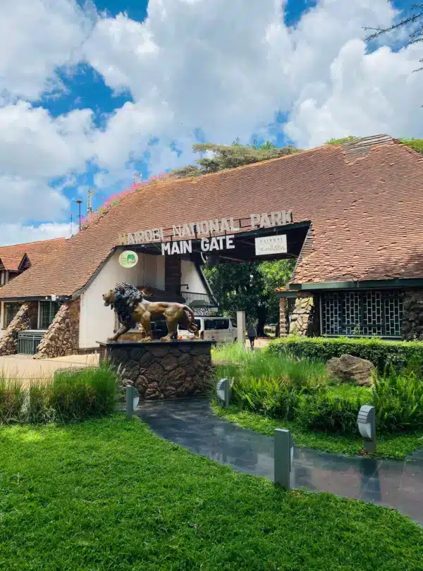 Main entrance of Nairobi National Park with lion statue and signage under a tiled roof.