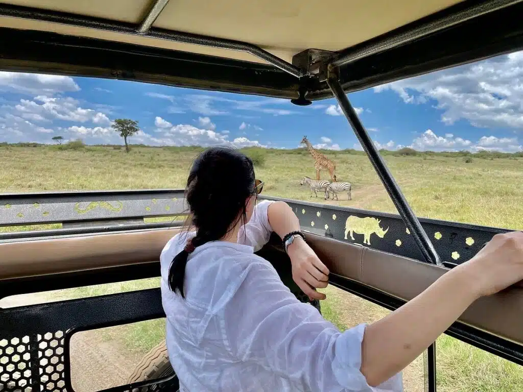 Guest enjoying private wildlife viewing from a safari vehicle in Kenya, watching giraffes and zebras during a game drive.