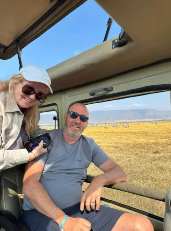 Couple enjoying game viewing during a 12-Day Kenya & Tanzania Safari with wildlife and crater rim scenery in the background
