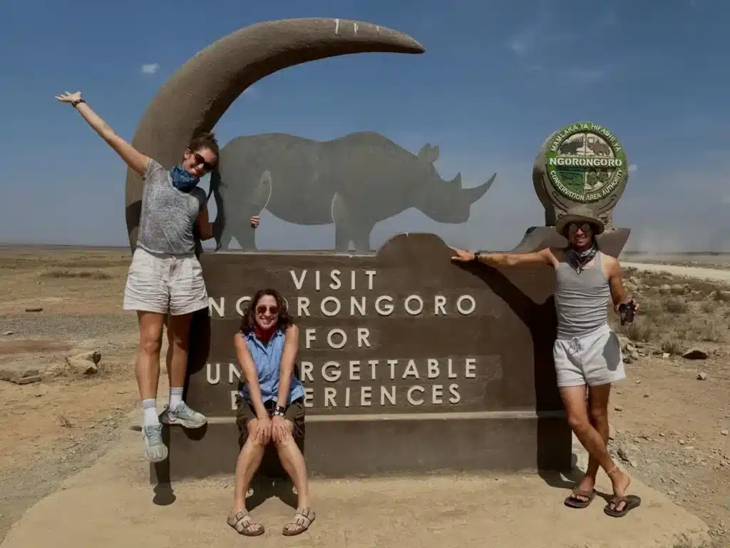 Travellers at the Ngorongoro Conservation Area entrance sign during a Tanzania safari.