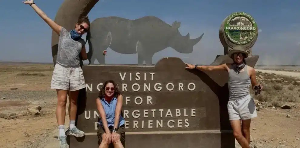 Travellers at the Ngorongoro Conservation Area entrance sign during a Tanzania safari.