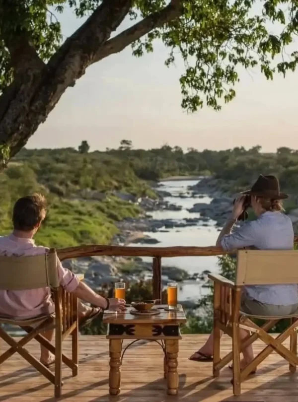 Two safari guests relaxing on a lodge deck overlooking a river in the Masai Mara, Kenya.